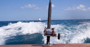 A fishing pole off the side of a charter boat with another boat riding closely behind.