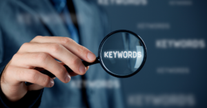 Photo of a man holding a magnifying glass over the word "Keywords"