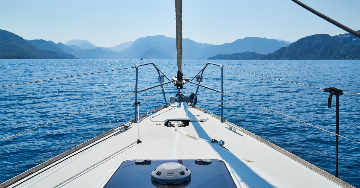 A sailboat sailing on a calm sea with mountains in the background.