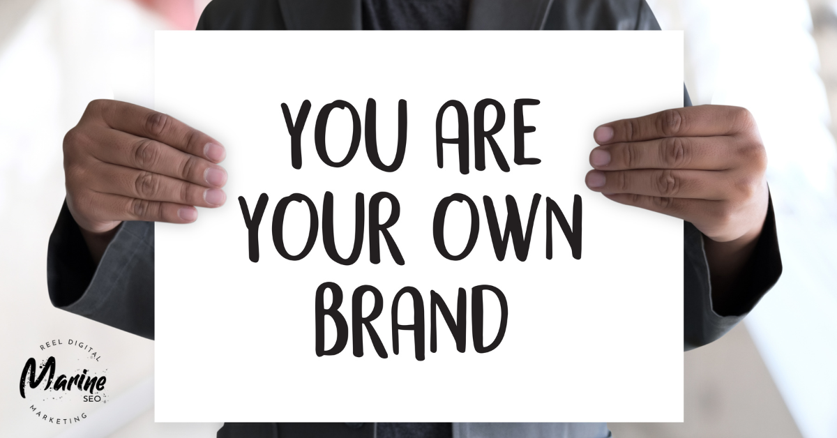 man holding a sign that says "you are your own brand"
