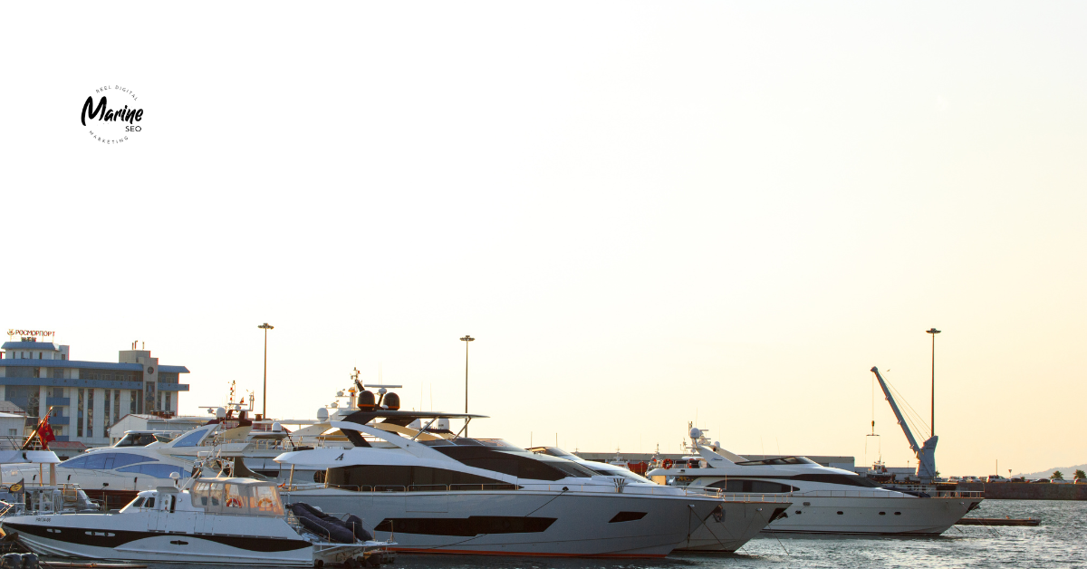 A row of luxury yachts docked at a marina during sunset, with calm water reflecting the boats and a faint Marine SEO logo in the sky above the scene.