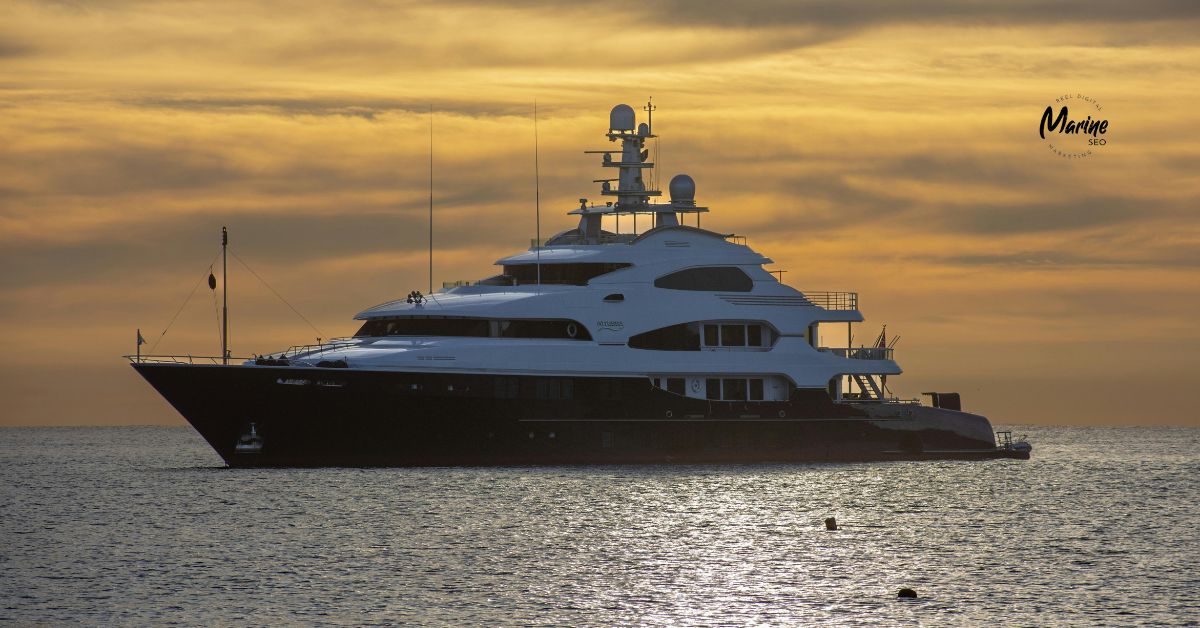 Luxury superyacht anchored on calm water at sunset, silhouetted against a golden sky with soft clouds and the Marine SEO logo in the upper right corner.