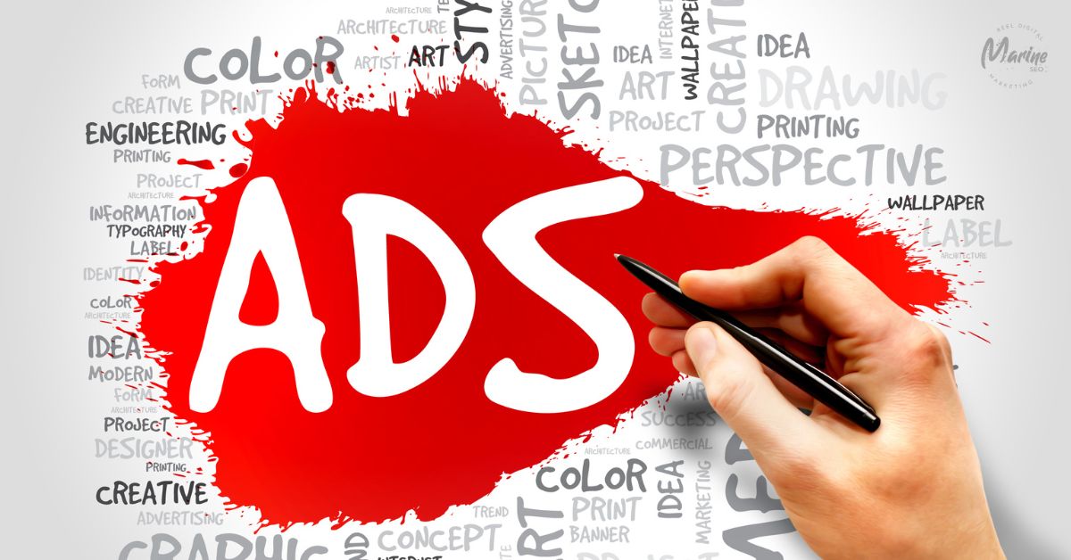 A hand holding a black pen pointing toward the word "ADS" written in large white letters inside a bright red paint splatter, surrounded by a word cloud of marketing and design terms.