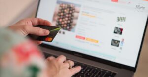 A person holding a black Mastercard while typing on a laptop keyboard to make a purchase on an online shopping website.